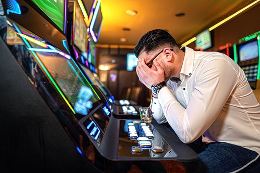 Worried man loosing his money on a slot machine in a casino.